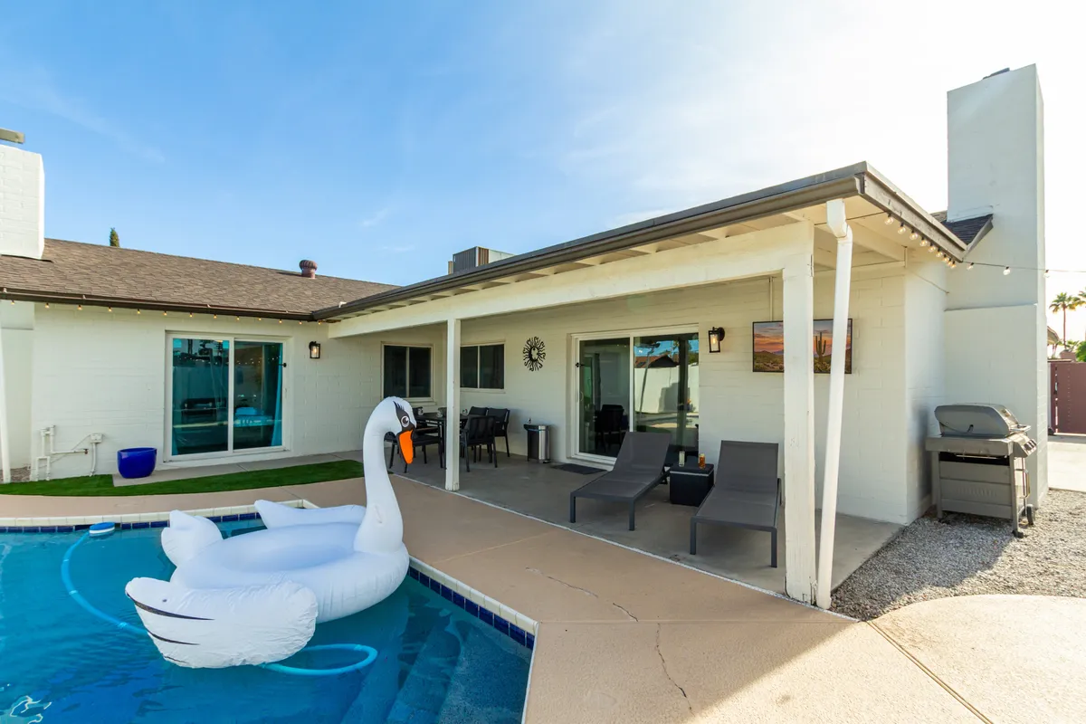 The image showcases a sparkling private pool with a whimsical swan float, surrounded by a stylish outdoor seating area and a built-in grill—perfect for socializing and relaxation. Lush landscaping and warm Arizona skies evoke a sense of resort-style luxury, with ample space for swimming, sunbathing, and outdoor dining.