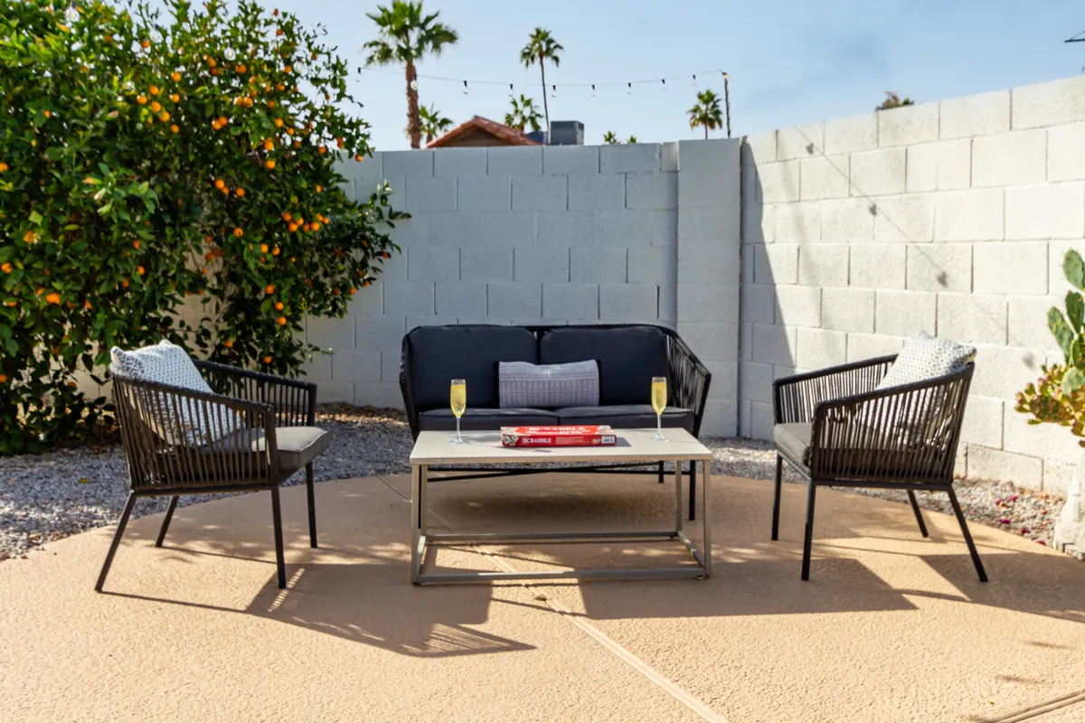 A stylish backyard oasis featuring an inviting outdoor seating arrangement around a coffee table, shaded by a leafy orange tree. The setting is perfect for relaxing, socializing, and soaking in the Arizona sunshine, embodying the concept of a private retreat.