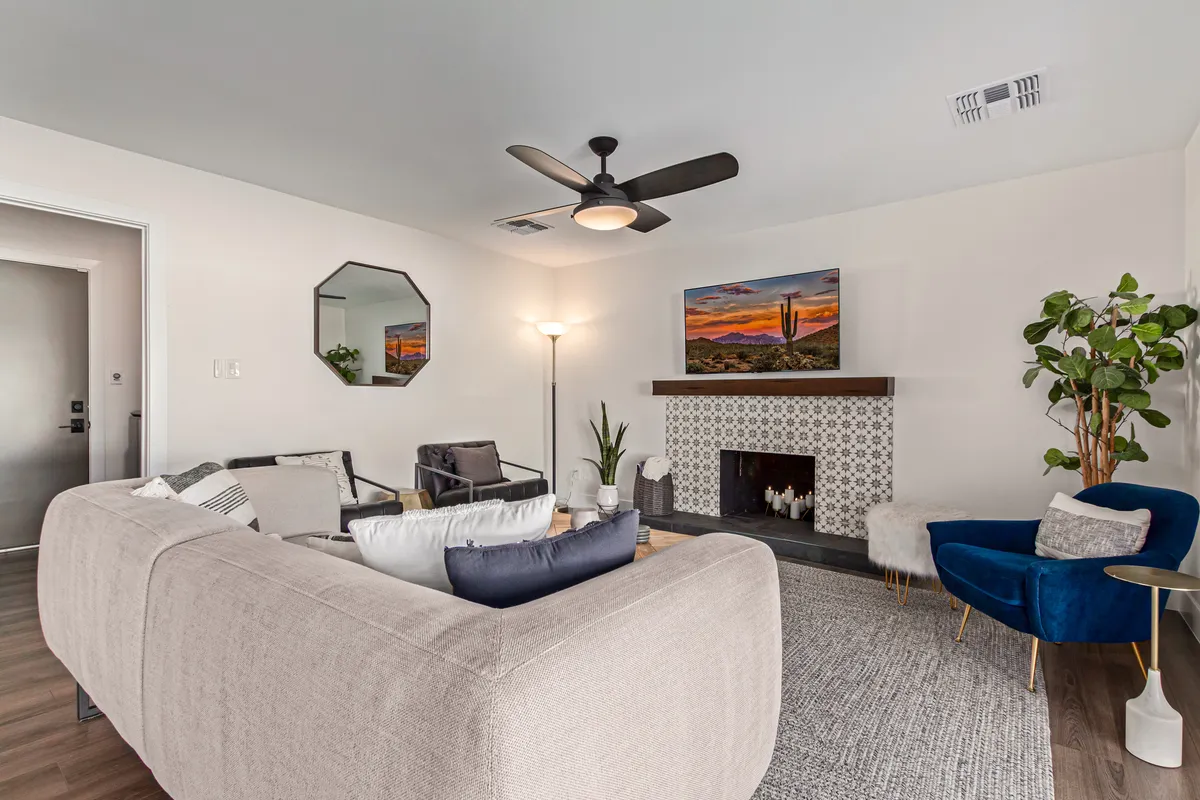 A spacious living area featuring a large sectional sofa, a modern fireplace, vibrant artwork, indoor plants, and ample natural light. The space is designed for relaxation and gathering, with cozy seating that encourages conversation and leisure. Modern lighting and stylish decor add to the contemporary, inviting feel.