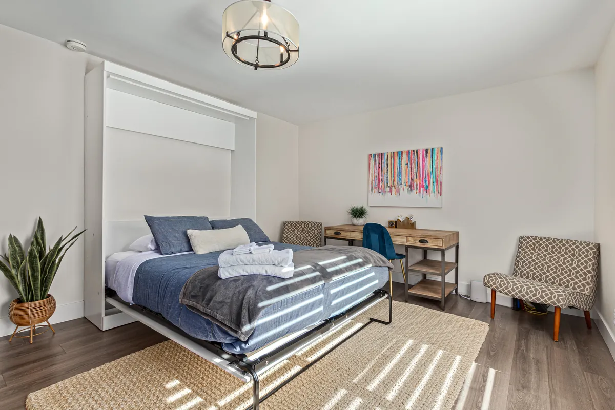 A serene Murphy bed room featuring a wall-mounted Murphy bed, a dedicated desk area for work or study, and tasteful modern decor. The space is well-lit and designed to support both relaxation and productivity.