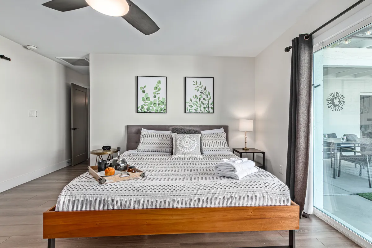 This image captures a bedroom with a bed adorned with decorative pillows, a side table with personal items, and wall art featuring plants. The atmosphere is calm and inviting, and natural light fills the space, suggesting privacy and comfort.