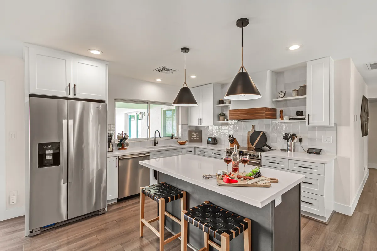 A contemporary kitchen with a generous island counter, stainless steel appliances, sleek pendant lighting, and open shelves with decorative items. The island features bar seating, ideal for casual breakfasts or engaging with the chef while cooking. The layout invites both culinary activity and conversation.